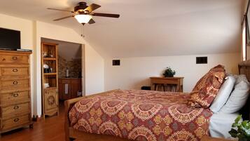 A bedroom with a wooden bed, a ceiling fan, a wooden dresser, and a small table with a plant.