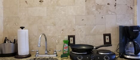 A kitchen with a granite countertop, stainless steel sink, a coffee maker, a frying pan, and a bottle of dish soap.