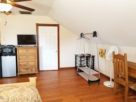 Un dormitorio con un aparador de madera, una cama, un escritorio con computadora, un ventilador de pie y un ventilador de techo.