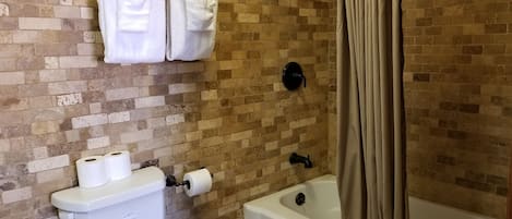 Een badkamer met een toilet, twee rollen toiletpapier, een douche met gordijn en handdoeken aan een rek.