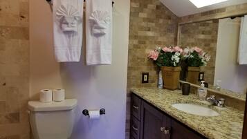 A bathroom with a toilet, two towels, a sink, a mirror, and a potted plant.