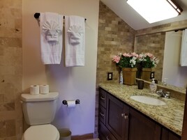 A bathroom with a toilet, two towels, a sink, a mirror, and a potted plant.