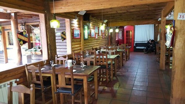 Un interior rústico de madera con varias mesas y sillas, piso de baldosas y lámparas colgantes.