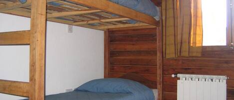 A bunk bed in a wooden cabin room with a window and a radiator.