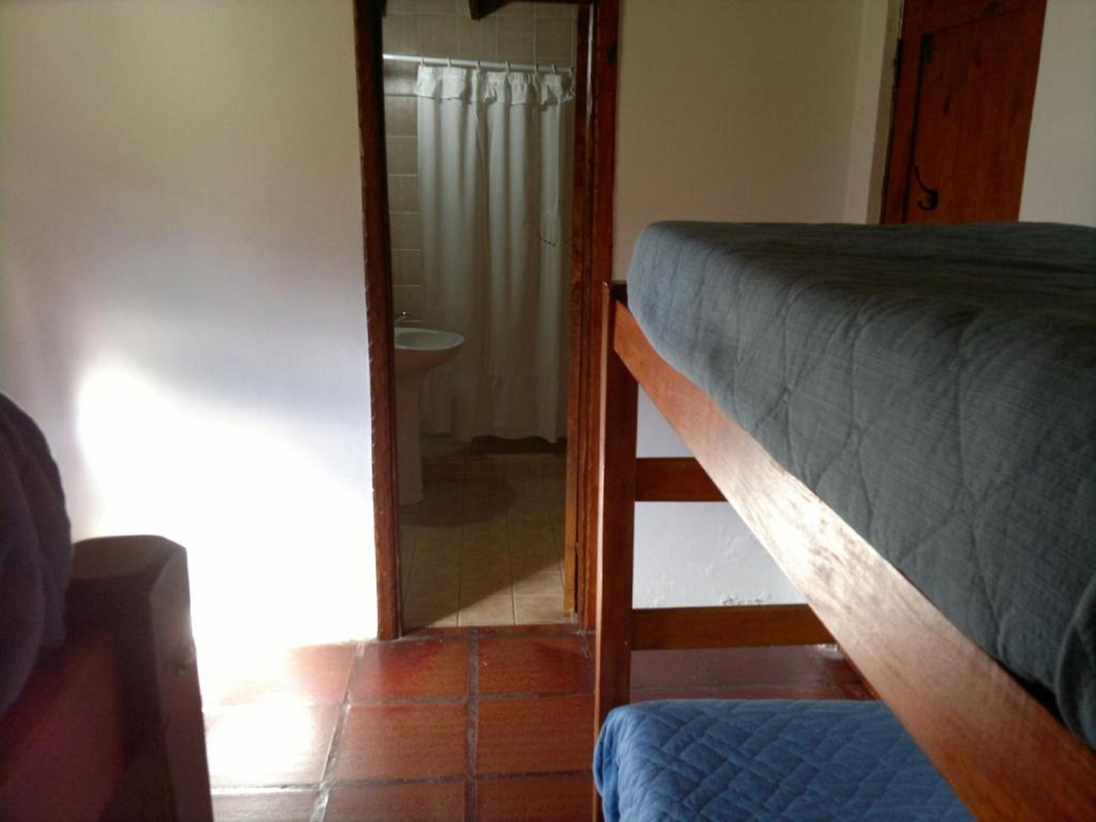 Un dormitorio con una cama de madera, un baño pequeño con lavamanos y un piso de baldosas.