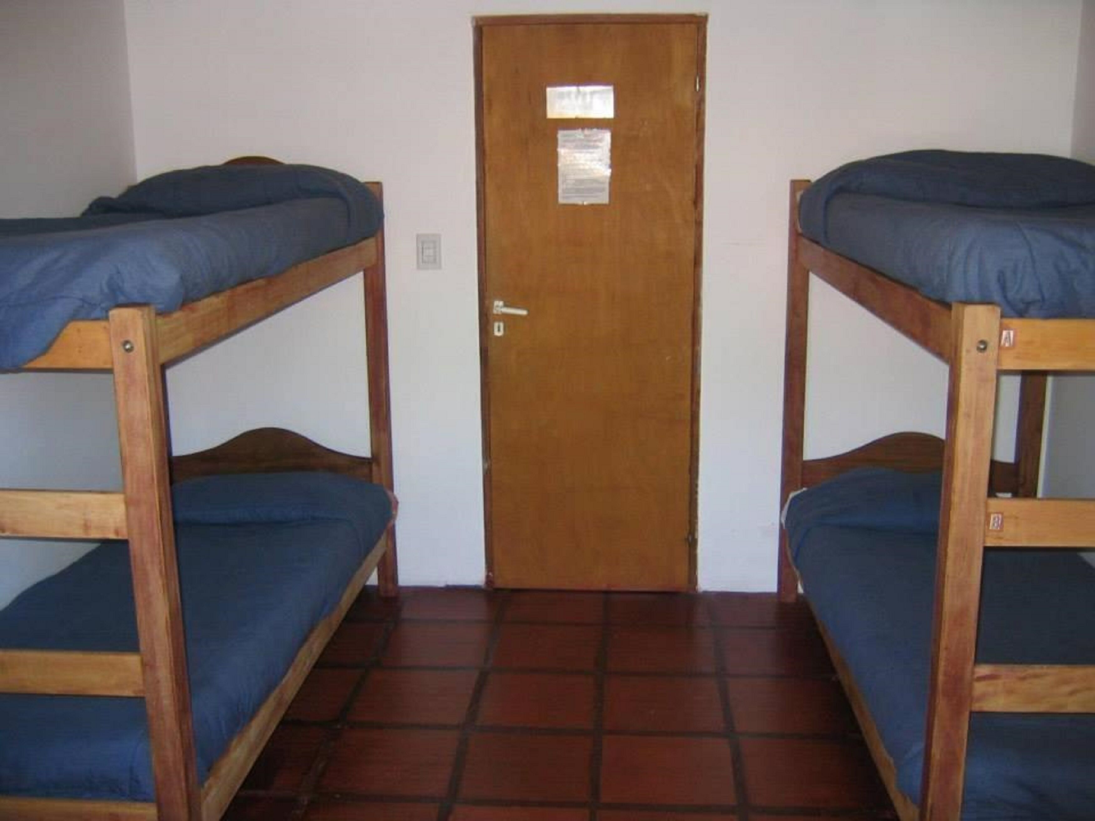 A room with two bunk beds, a wooden door, and a tiled floor.