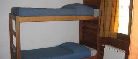 A bunk bed with blue bedding in a cabin-style room with wooden walls and a window with yellow curtains.