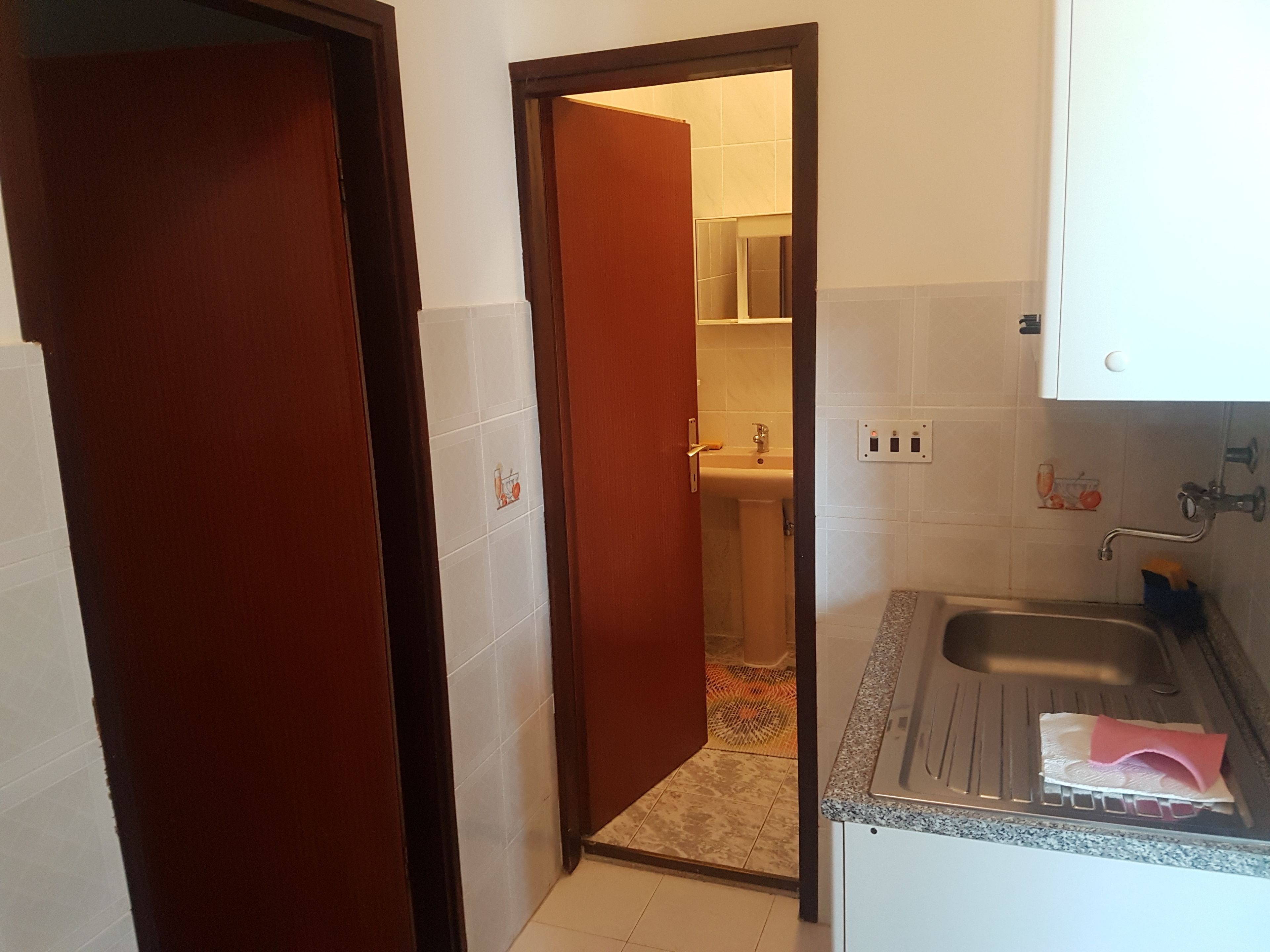 A narrow bathroom with a sink, a towel, and a door leading to a bathroom area.