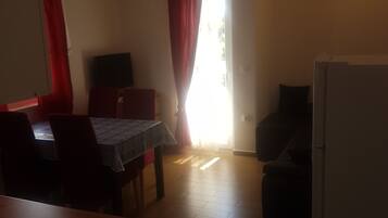 A kitchen with a refrigerator, a dining table with chairs, and a window with curtains.