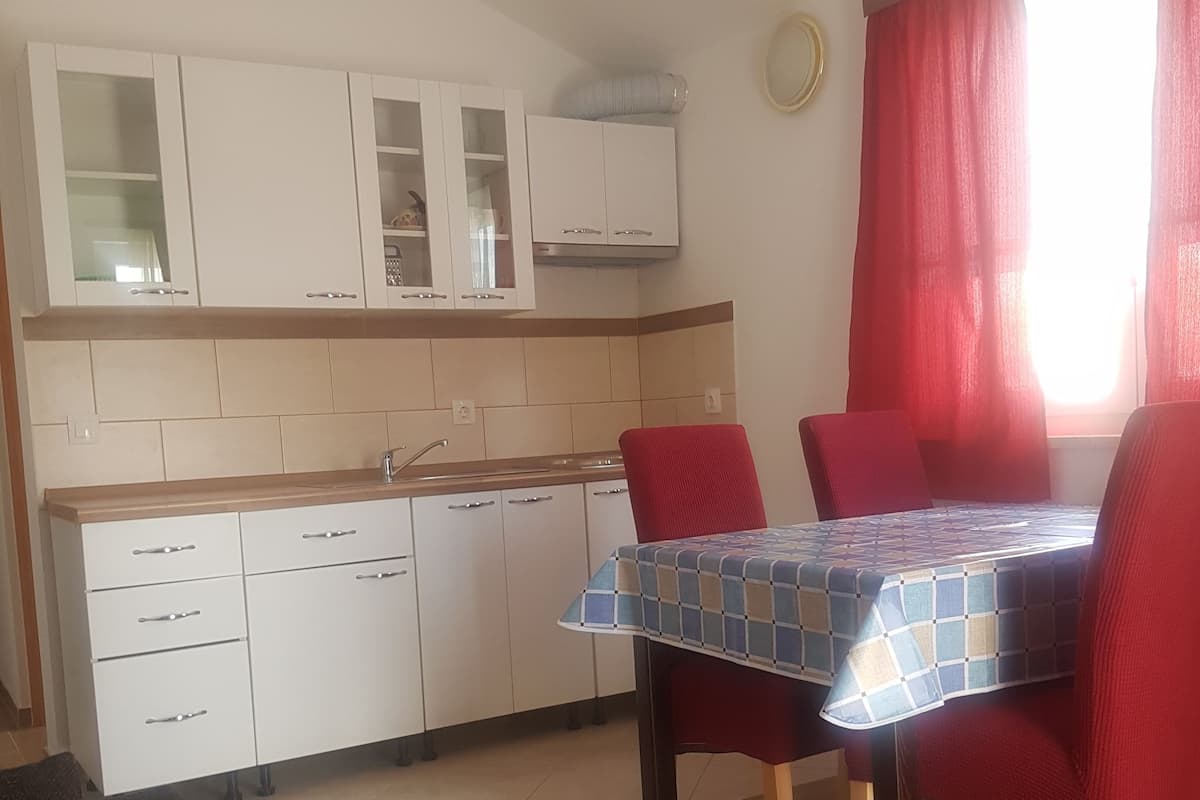 Une cuisine de taille modeste avec des meubles blancs, une table à manger recouverte d’une nappe à carreaux et des chaises rouges.
