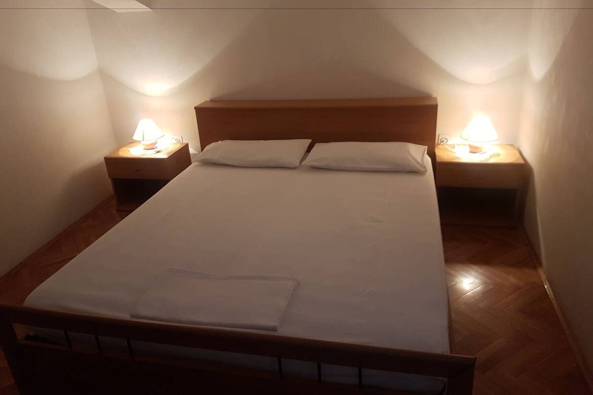 Un lit bien fait, avec du linge de lit blanc et deux lampes de chevet posées sur des tables de nuit en bois.