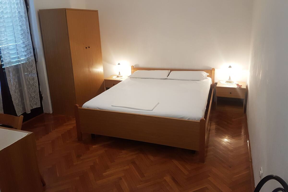 Une chambre à coucher avec un lit en bois, deux lampes de chevet, une armoire et une fenêtre avec un rideau.