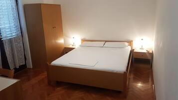 Un dormitorio con una cama de madera, dos lámparas de noche, un armario y una ventana con cortina.
