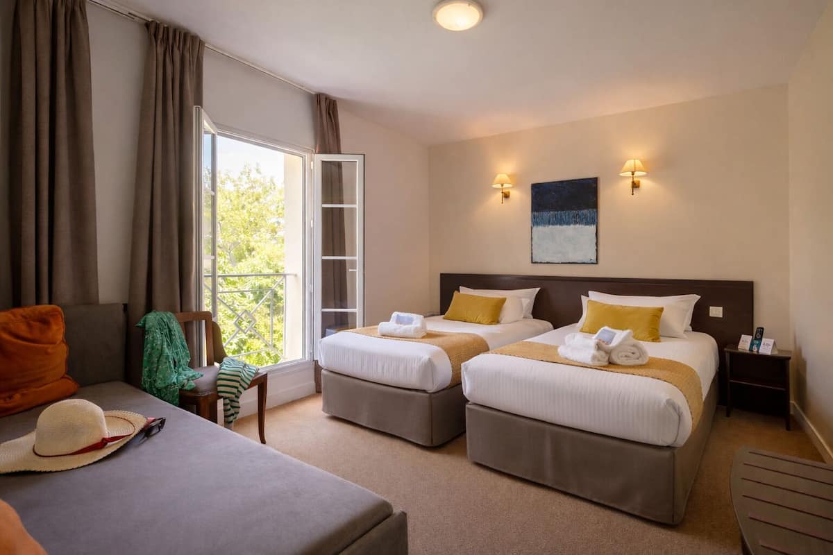 A hotel room with two beds, a sofa, a chair, a balcony, and a painting on the wall.