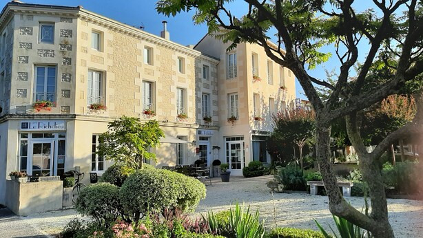 Un edificio histórico con una cafetería llamada "Le Richelieu" en la planta baja, rodeado de jardines cuidados y un camino de grava.