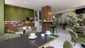 Una cafetería moderna con paredes verdes, detalles de madera y diferentes opciones de asientos.