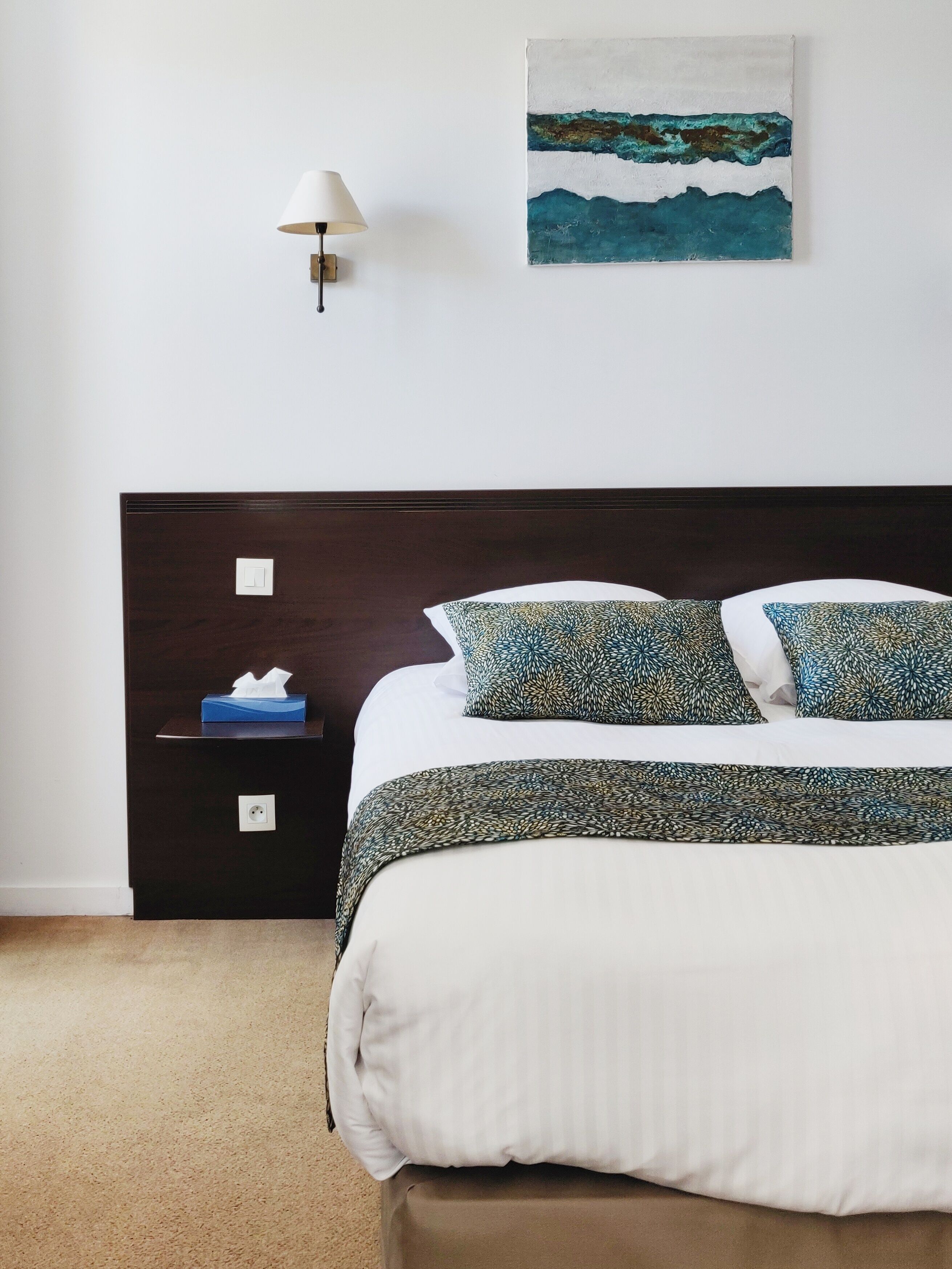 Une chambre à coucher bien rangée, avec un lit, une table de chevet dotée d’une lampe et un tableau accroché au mur.