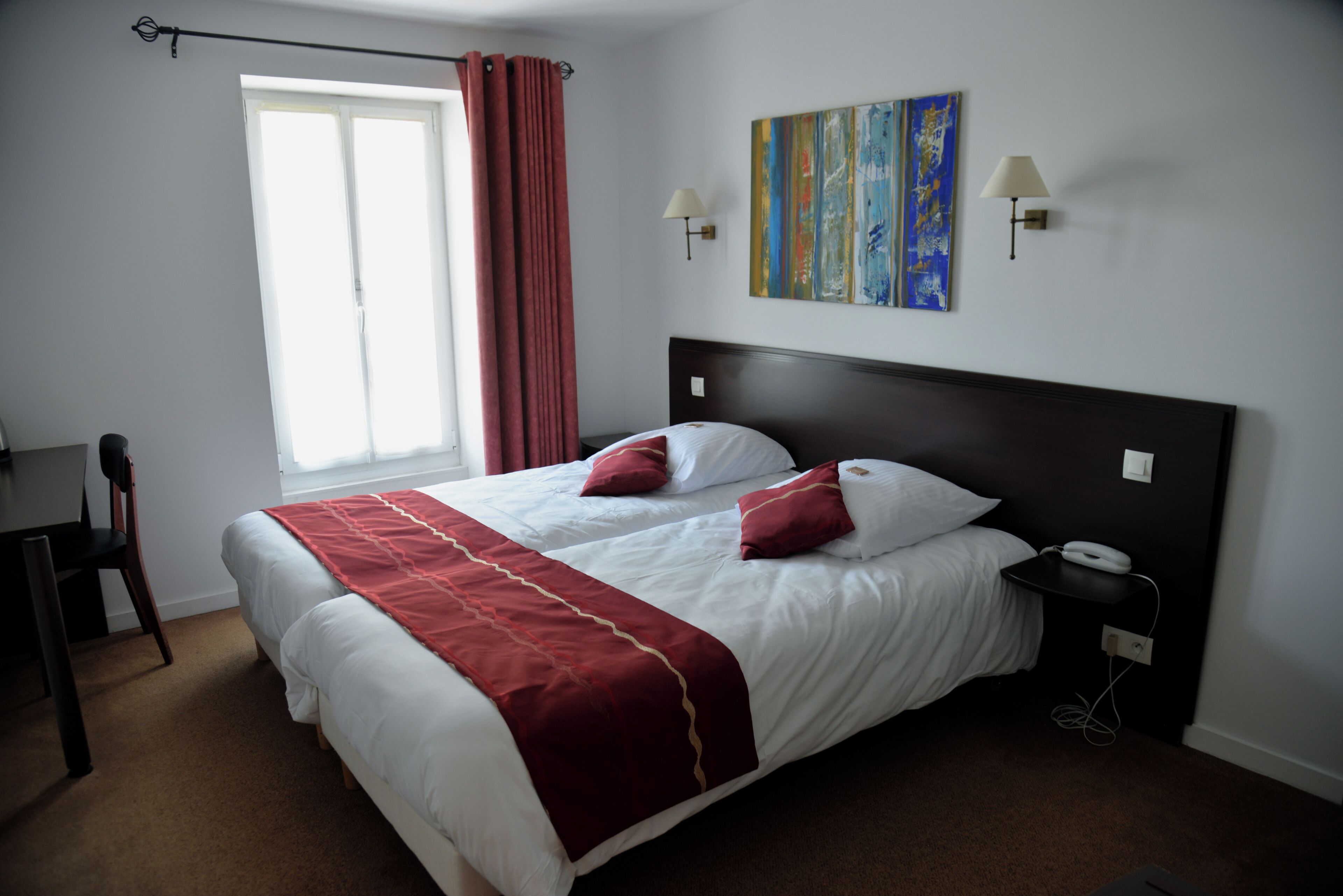 Habitació d'hotel amb un llit gran, dues làmpades de nit, una tauleta de nit, un escriptori i una finestra amb cortines.
