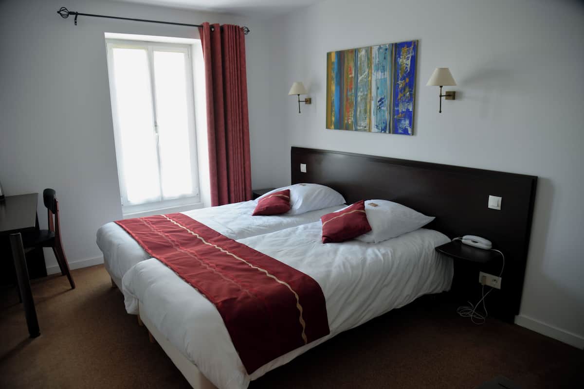 A hotel room with a large bed, two bedside lamps, a nightstand, a desk, and a window with curtains.