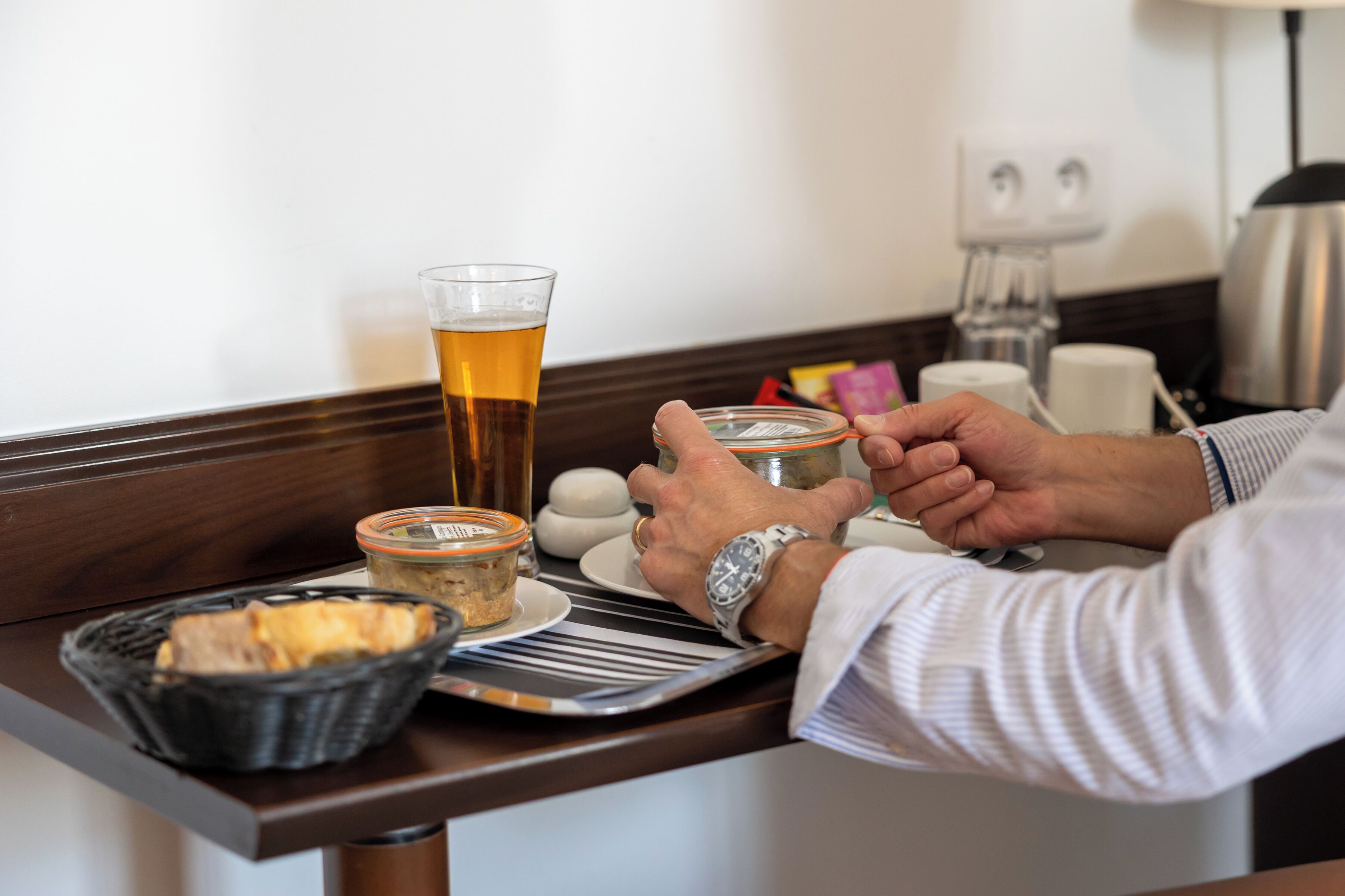 Une chambre d’hôtel avec un buffet en bois, un verre de bière, un panier de pain et un pot de confiture.