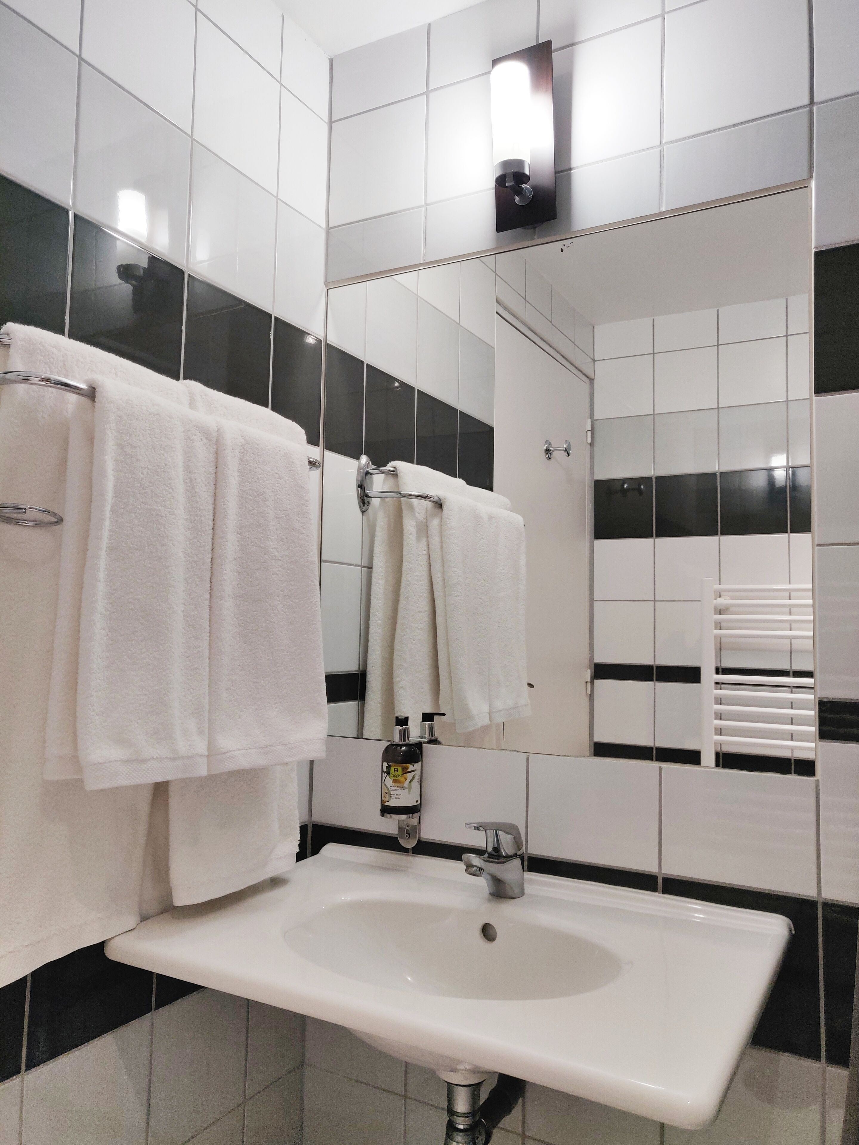 Une salle de bain avec un lavabo blanc, des murs carrelés en noir et blanc, et un miroir au-dessus du lavabo.