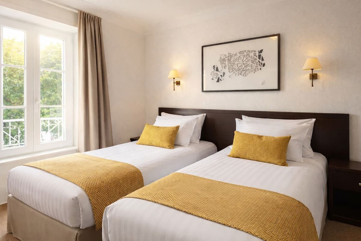 A hotel room with two beds, each with white linens and a yellow throw. There are two wall-mounted lamps and a framed abstract artwork above the beds.