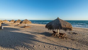 A beach with thatched umbrellas and wooden chairs, a clear sky, and the ocean in the background. - Luna Blanca Villa 07 by Kivoya (Puerto Peñasco)