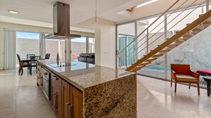 A spacious kitchen with granite countertops, a central island, and a modern staircase leading to a balcony. - Luna Blanca Villa 07 by Kivoya (Puerto Peñasco)