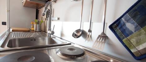 A kitchen with stainless steel appliances, including a stove, sink, and hanging utensils.