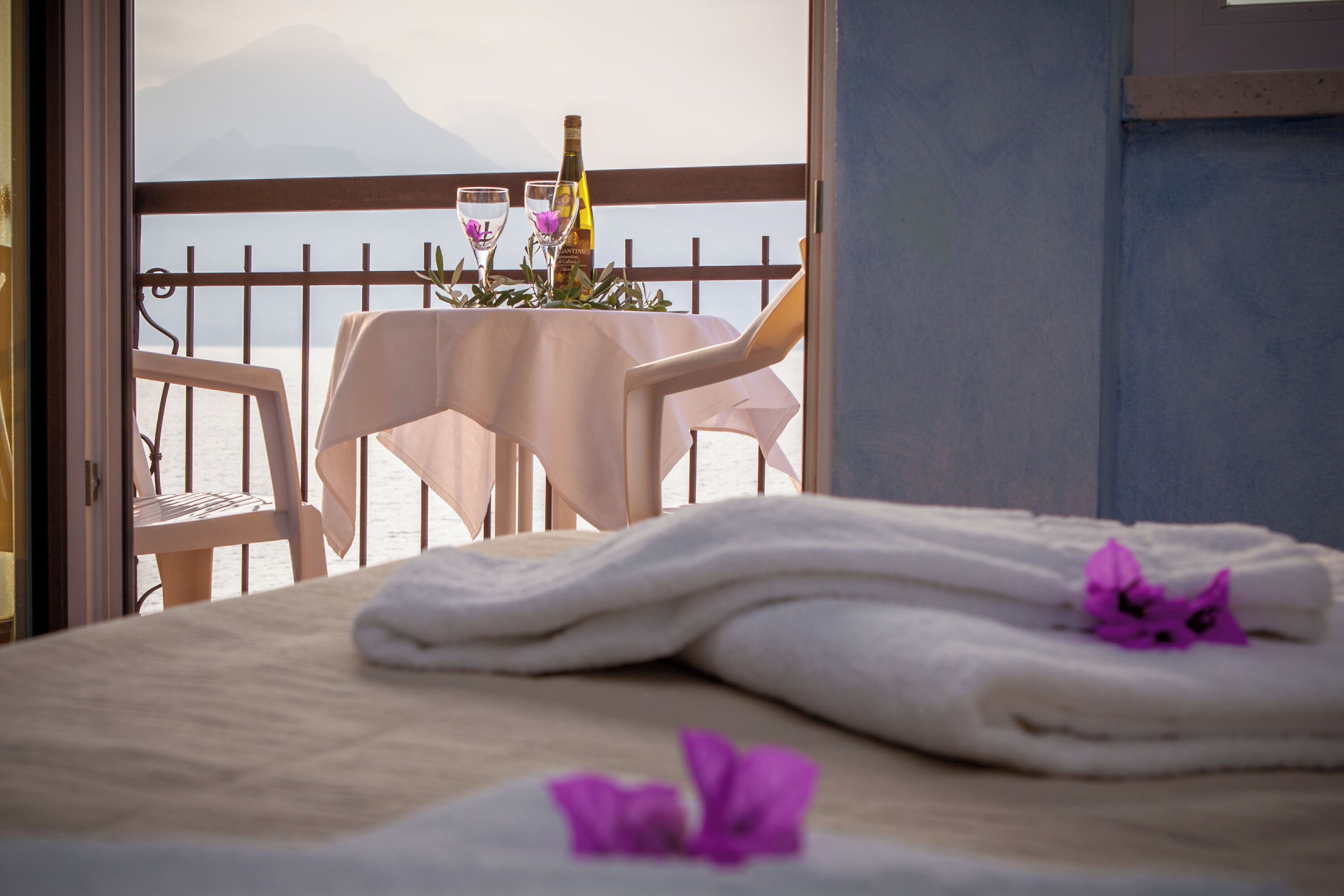 A balcony with a table set for two, overlooking a body of water and a mountain.