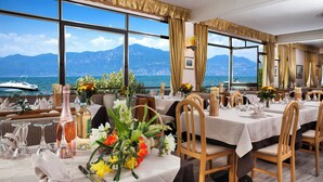 Un restaurante con mesas dispuestas para comer, amplias ventanas con vistas al mar y las montañas, y diferentes tipos de mantelería.