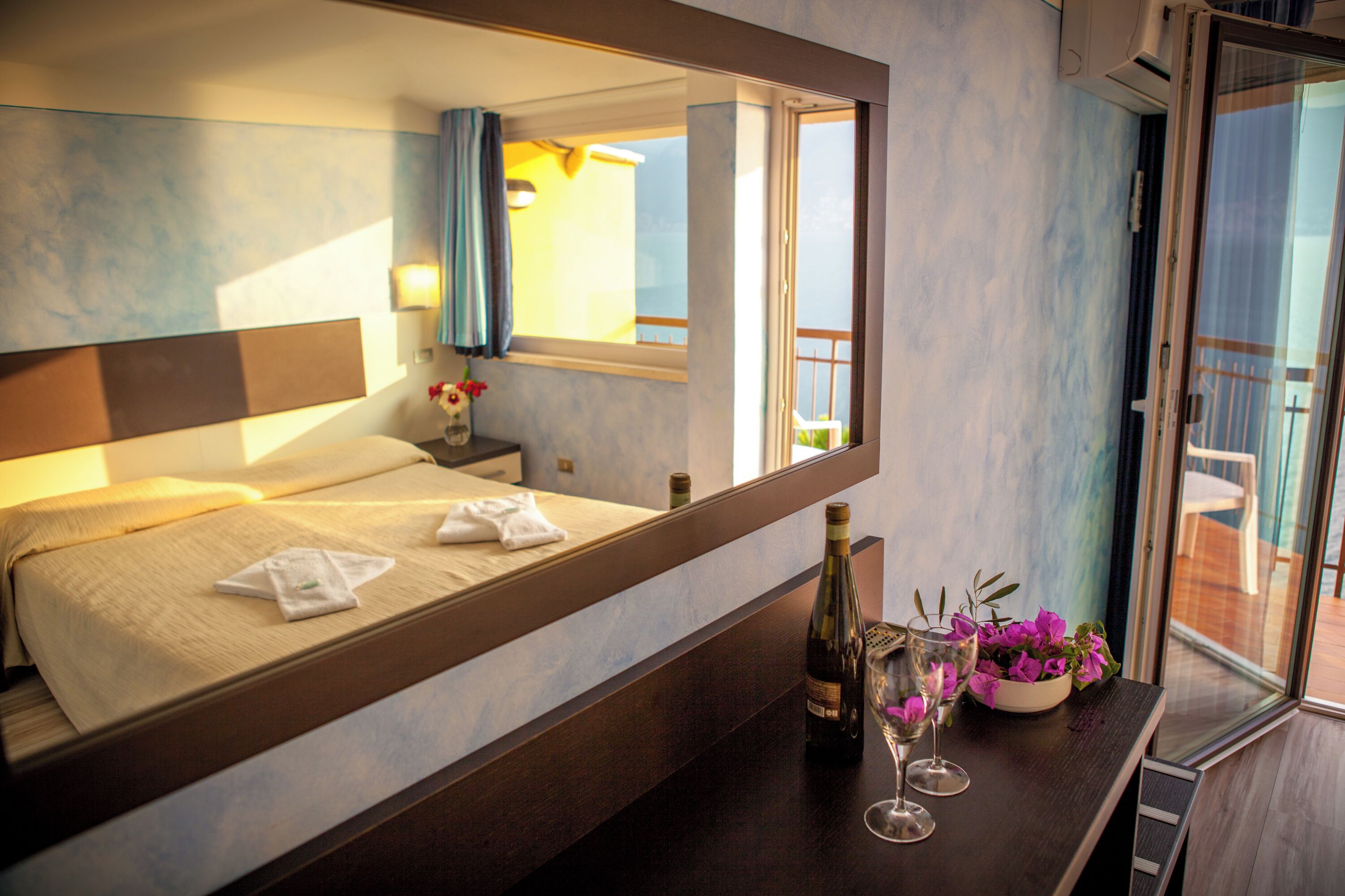 A hotel room with a bed, a nightstand, a vase with flowers, a bottle of wine, and a glass.