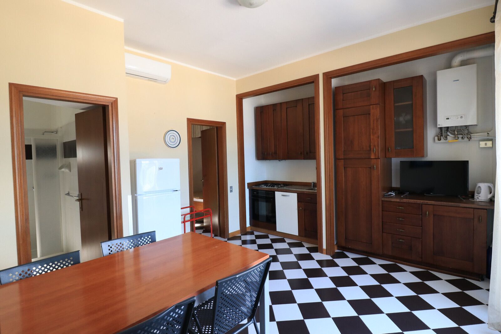 A compact kitchen with wooden cabinets, a refrigerator, a stove, and a television.
