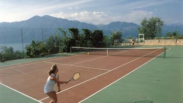 Ein Tennisplatz mit Netz, umgeben von einem Zaun und Bäumen.