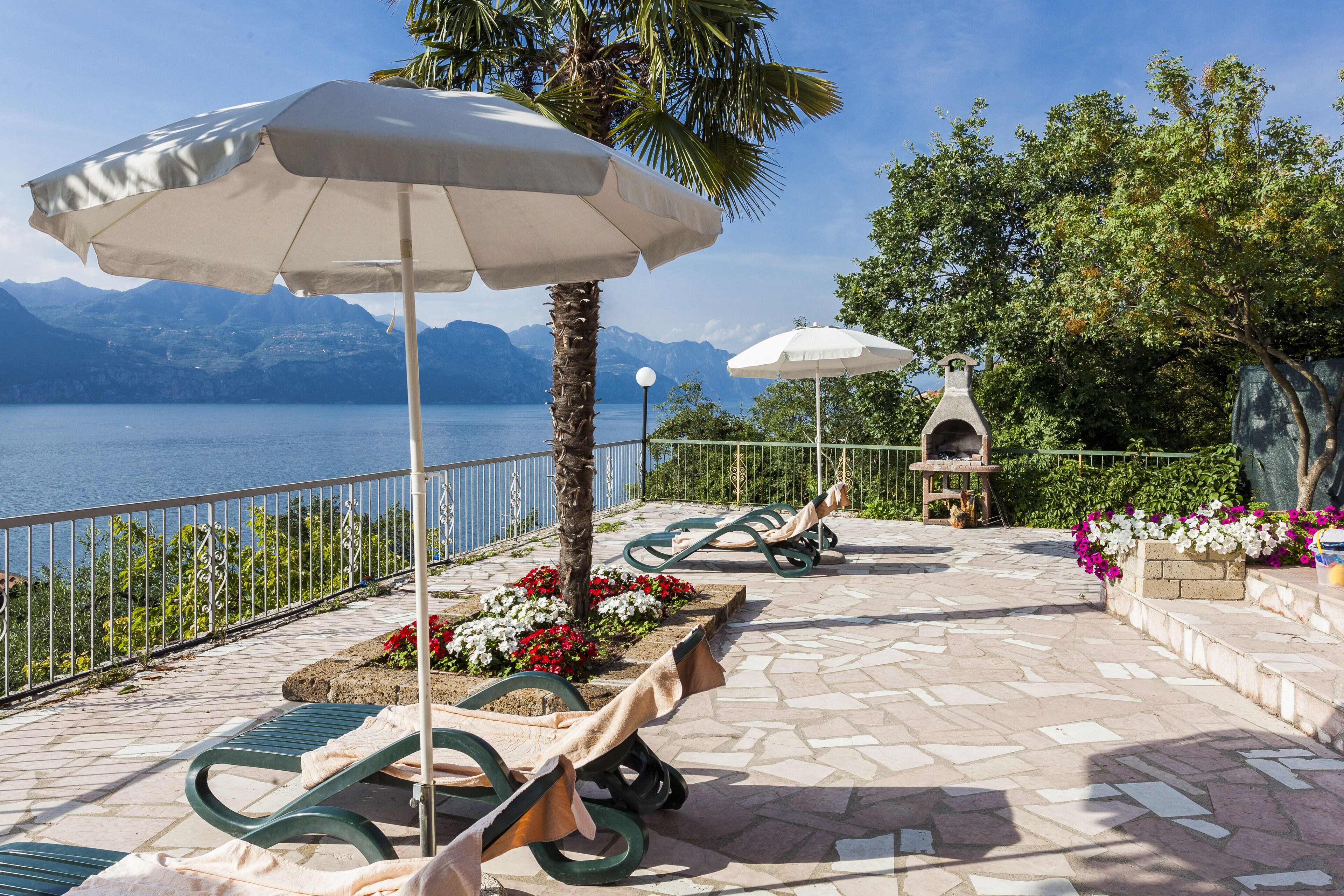 Una terrazza con posti a sedere all'aperto, ombrelloni e vista su un lago con montagne sullo sfondo.
