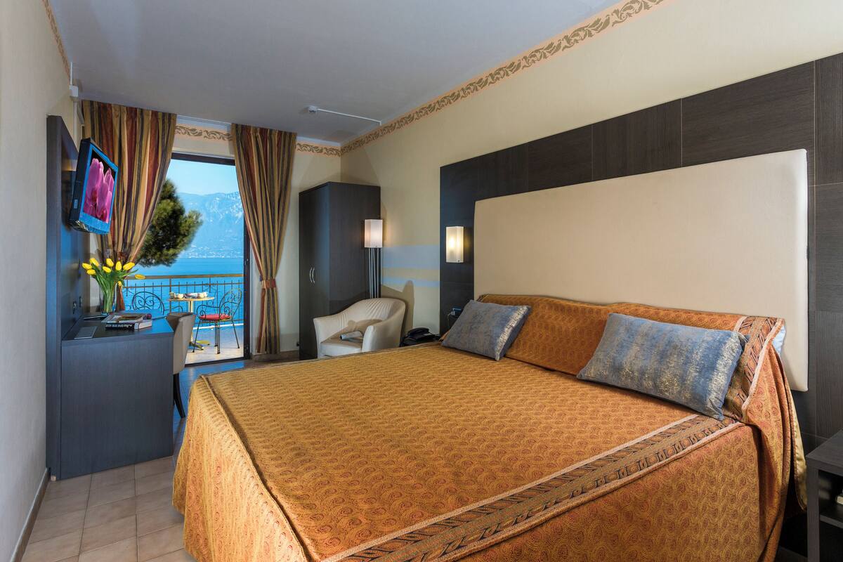 Une chambre d’hôtel avec un grand lit, un bureau avec une chaise, une télévision et une vue sur la mer.