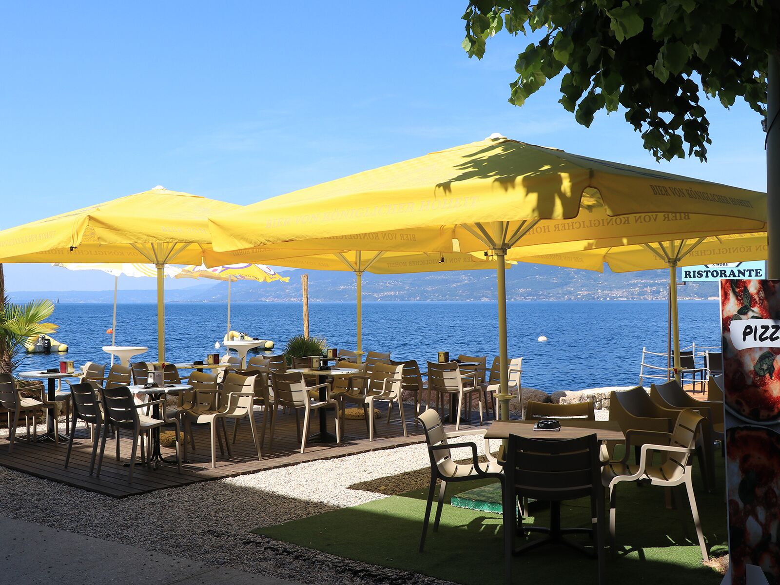 Outdoor seating with yellow umbrellas, a view of the sea, and a sign for a restaurant.