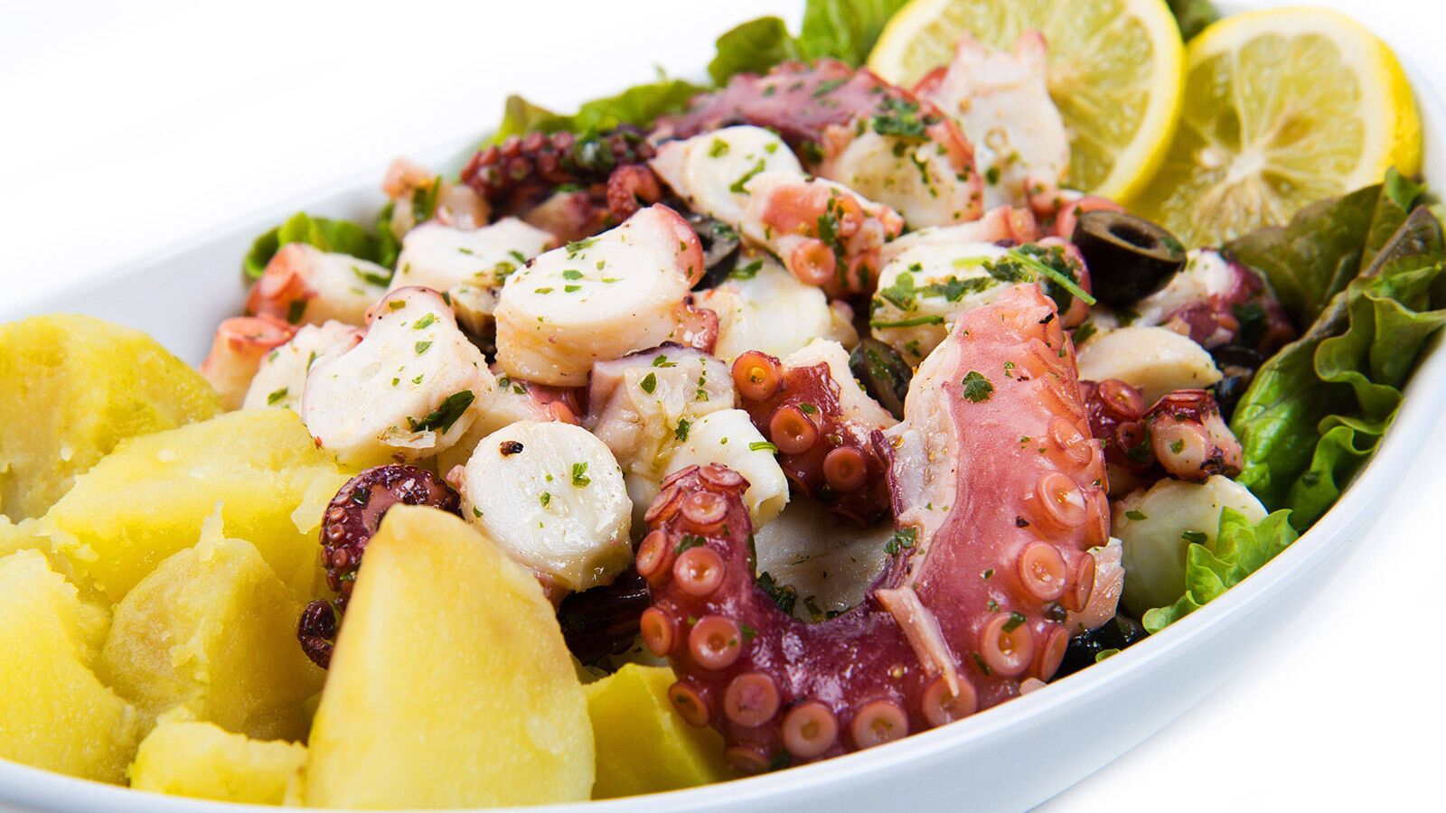 Un plato de pulpo, patatas y verduras de hoja verde.