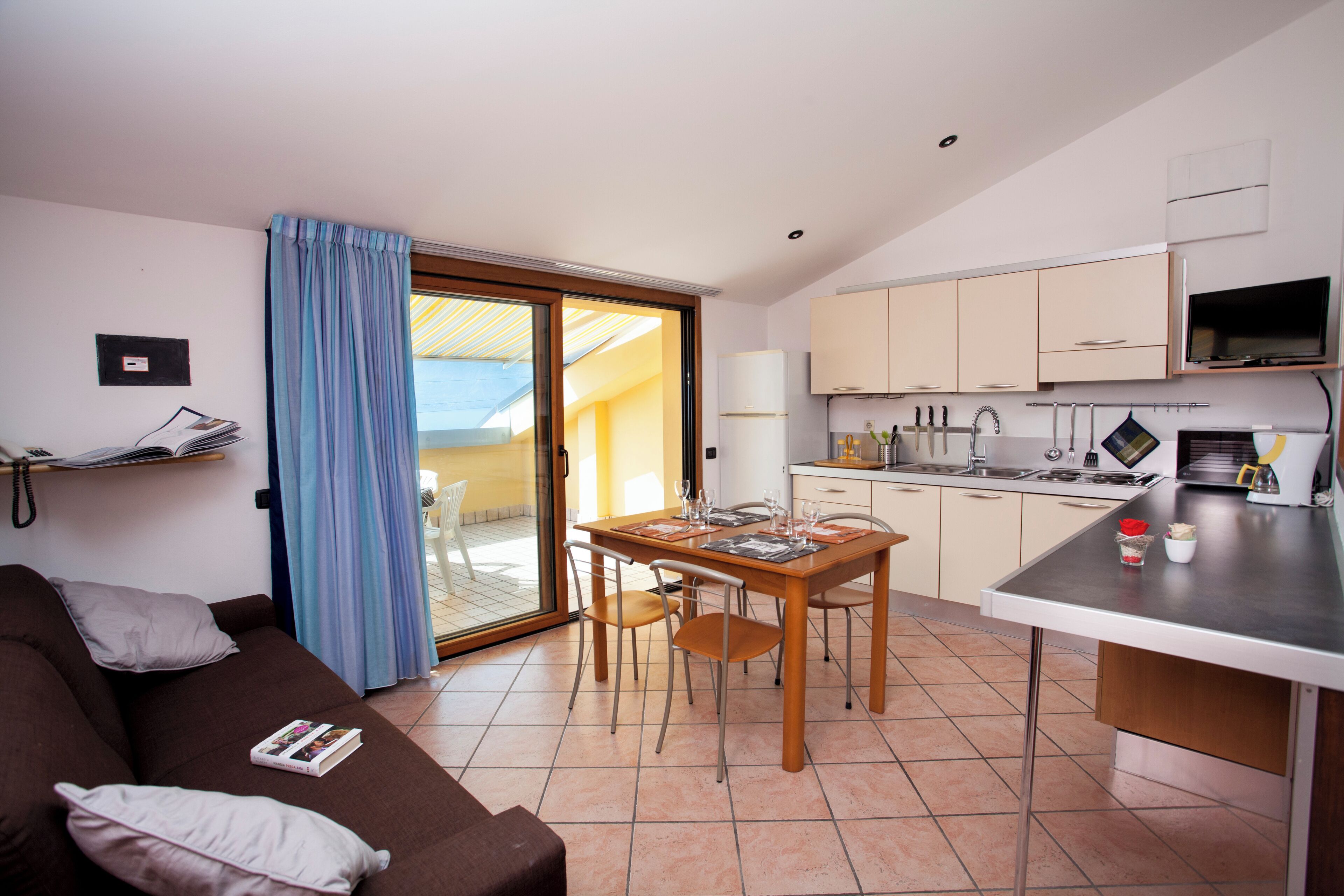 Un espacio habitable compacto con kitchenette, zona de comedor y puerta corrediza de vidrio que da a un área exterior.