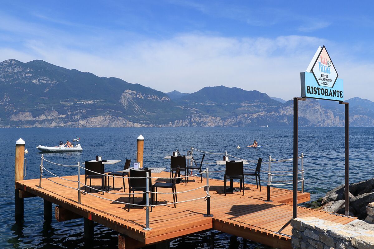 A wooden dock with chairs and tables, a sign for a restaurant, and a mountainous backdrop.