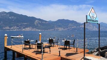 A wooden dock with chairs and tables, a sign for a restaurant, and a mountainous backdrop.