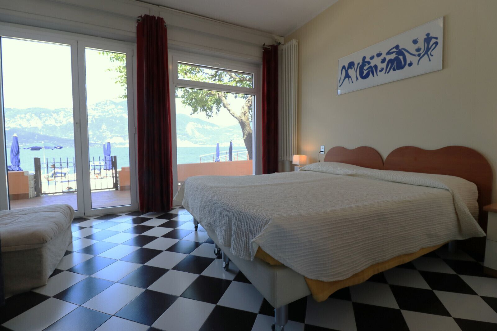 Quarto de hotel com cama, uma cadeira, vista para o mar e um quadro na parede.
