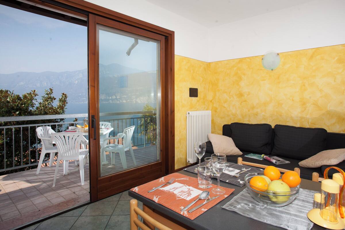 Un coin repas avec une table dressée pour deux personnes, un canapé et une vue sur la mer.