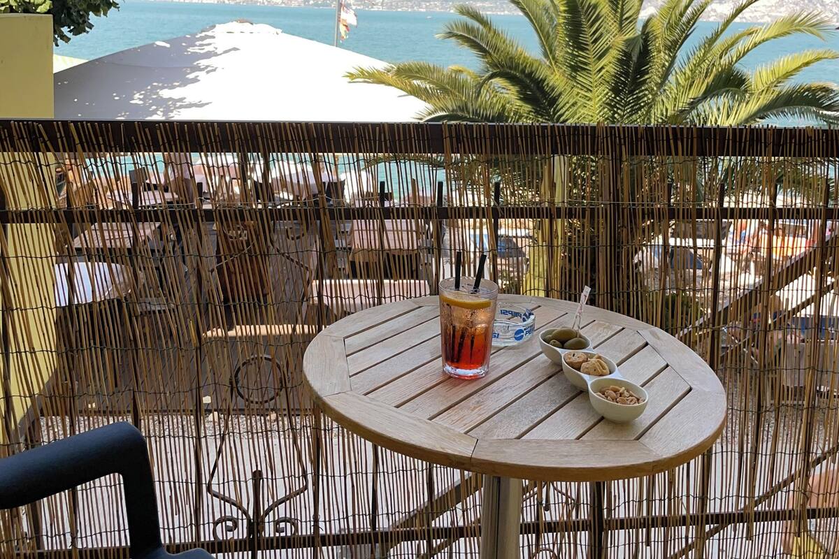 Une table ronde avec des boissons et des biscuits, une chaise, et une vue sur la mer et les montagnes.