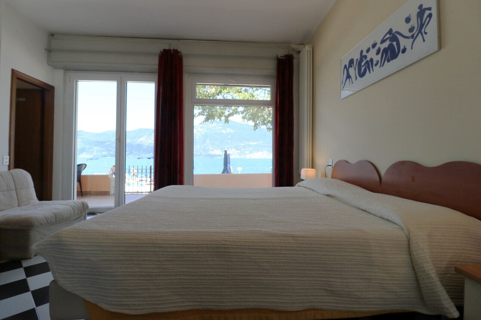 Habitación de hotel con una cama grande, un sofá, un balcón con vista al mar y un cuadro en la pared.
