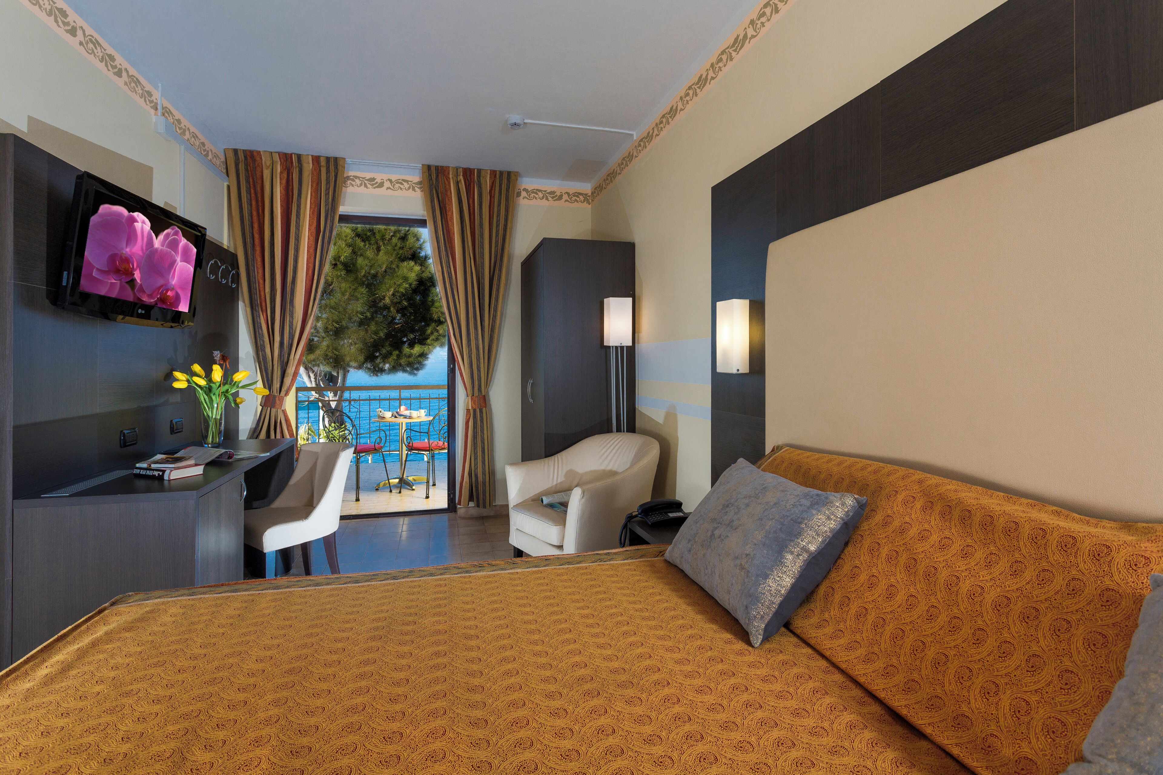 A hotel room with a bed, a desk, a chair, a TV, and a view of the outdoors.