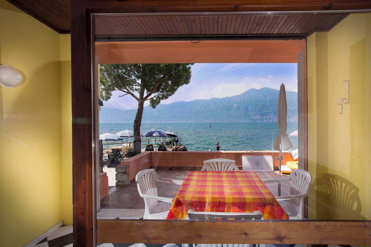 Un coin repas avec une table et des chaises, donnant sur une étendue d’eau et offrant une vue sur des montagnes en arrière-plan.