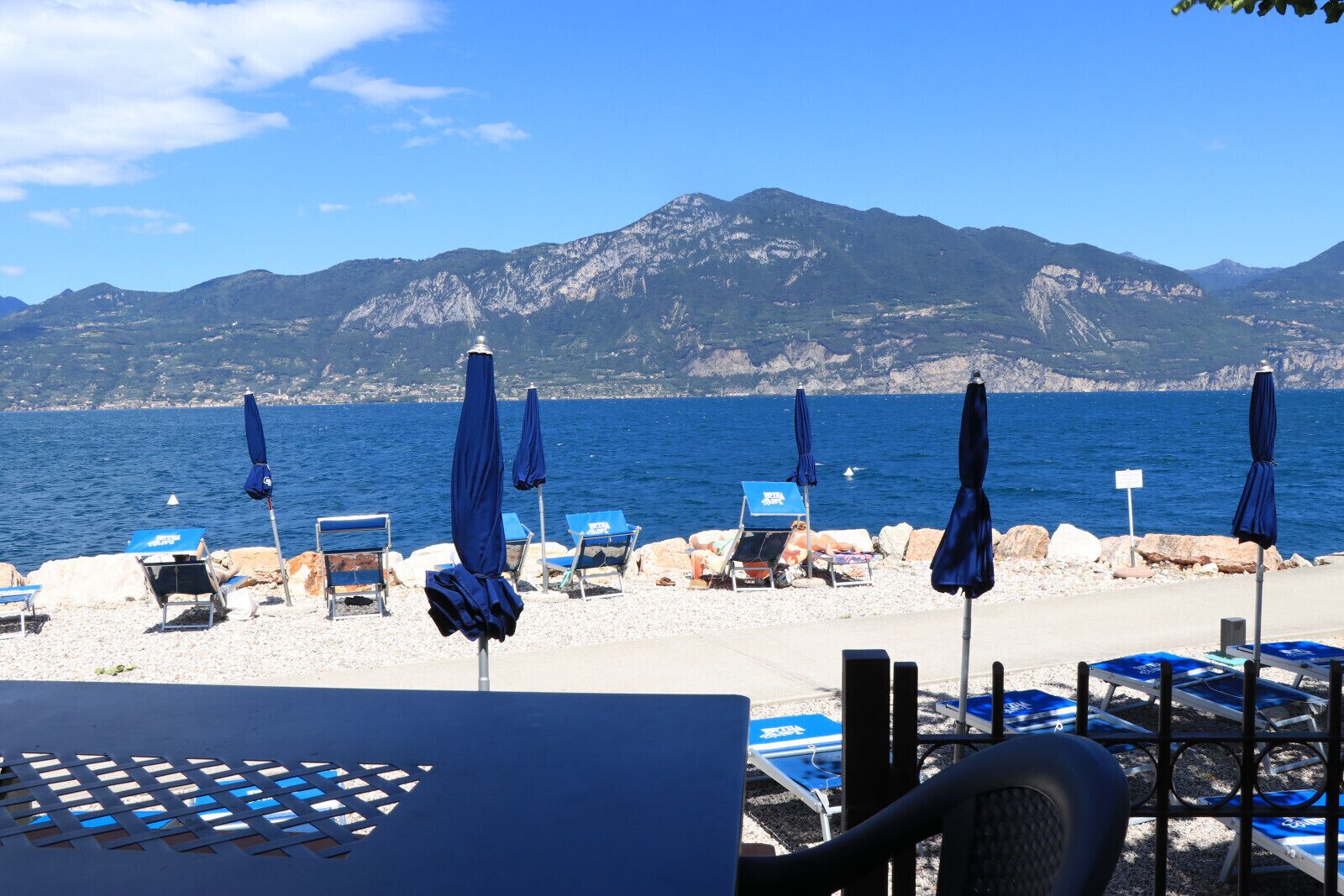 A beach with umbrellas and lounge chairs, a rocky shoreline, and mountains in the background.