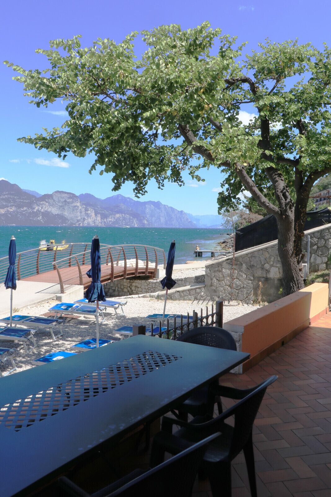 A terrace with a table and chairs, a tree, and a view of the sea and mountains.