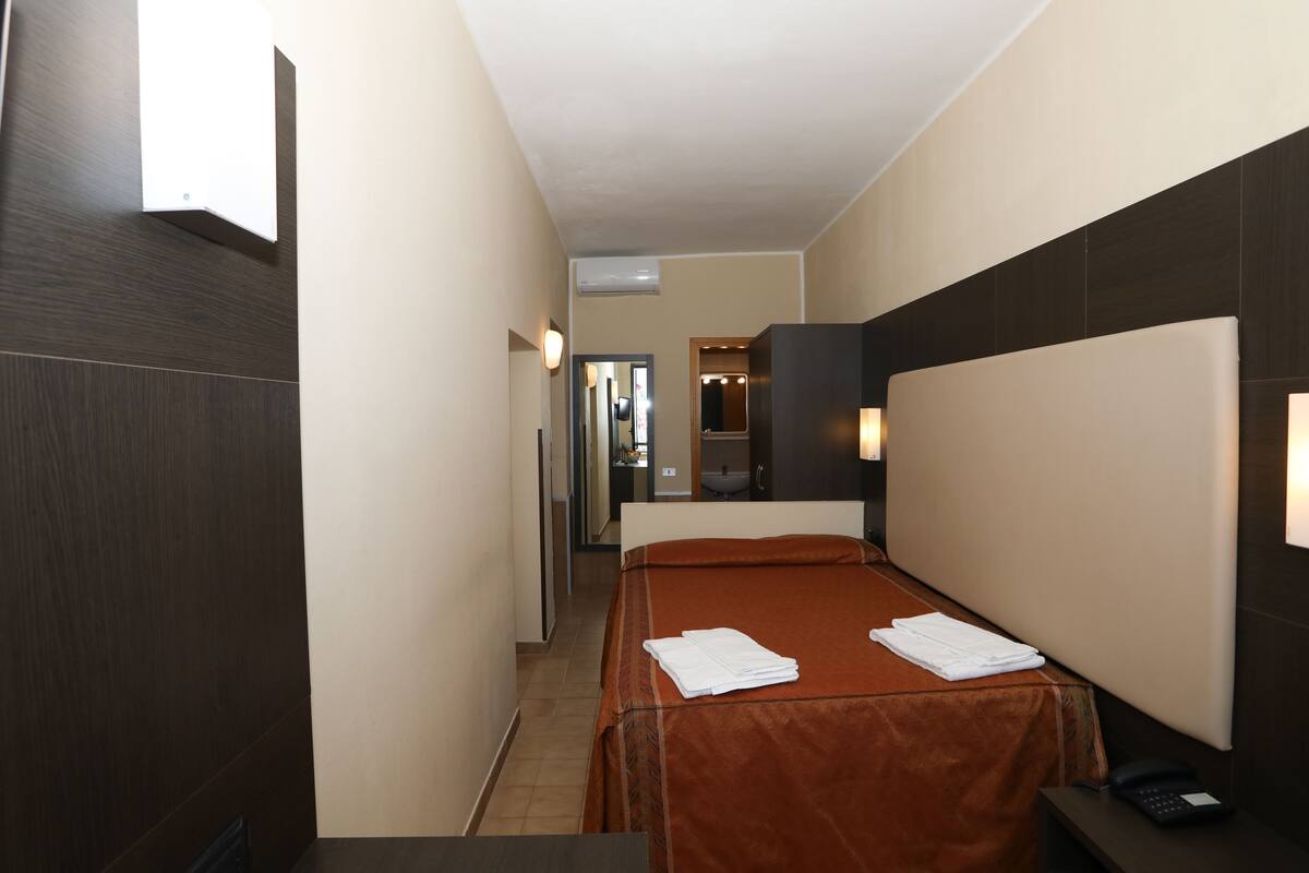 Une chambre d’hôtel avec un lit simple, une table de chevet, un téléphone et un miroir.